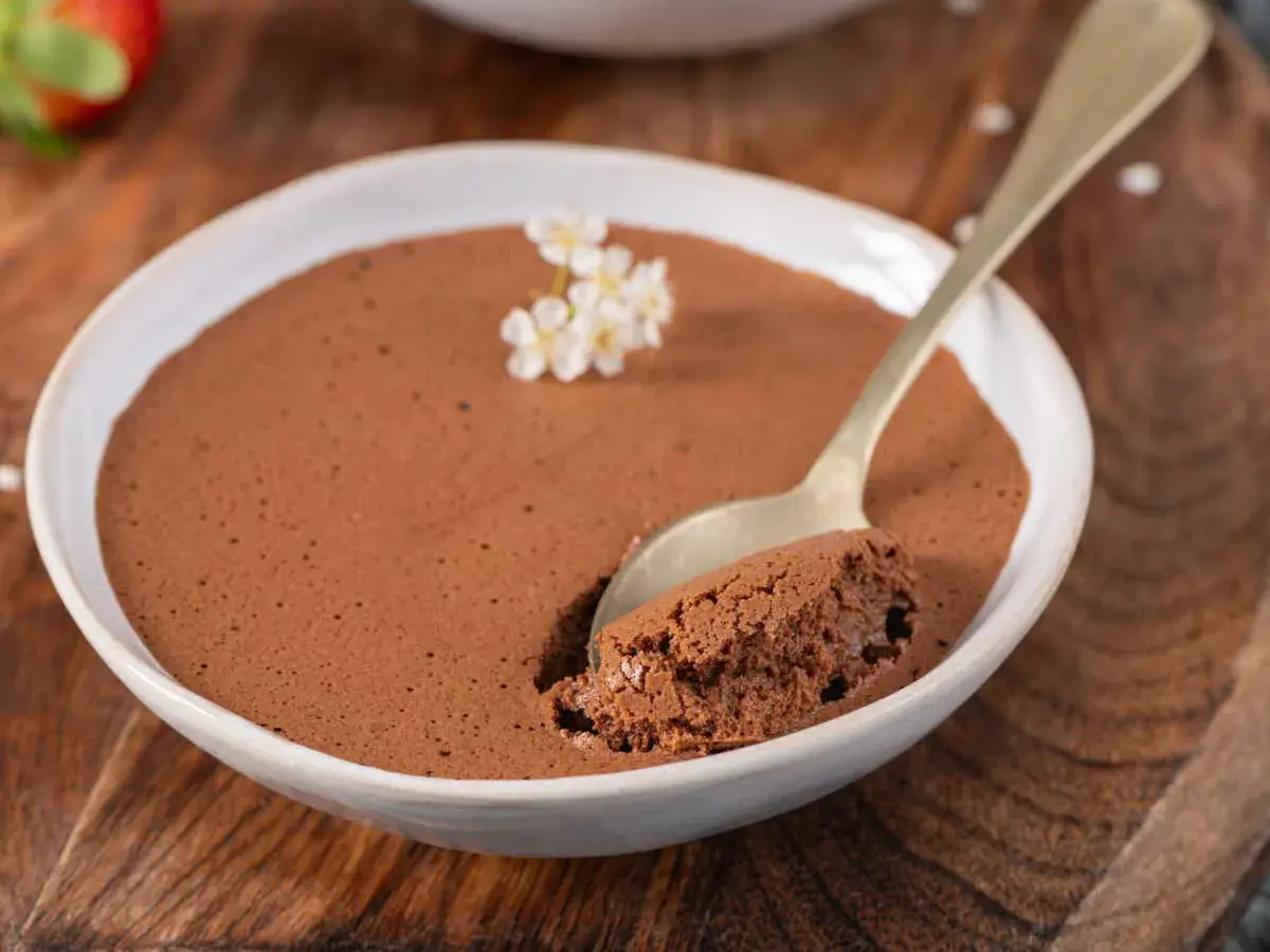 Une cuillère prend une bouchée d'une délicieuse mousse au chocolat, garnie de petites fleurs blanches.