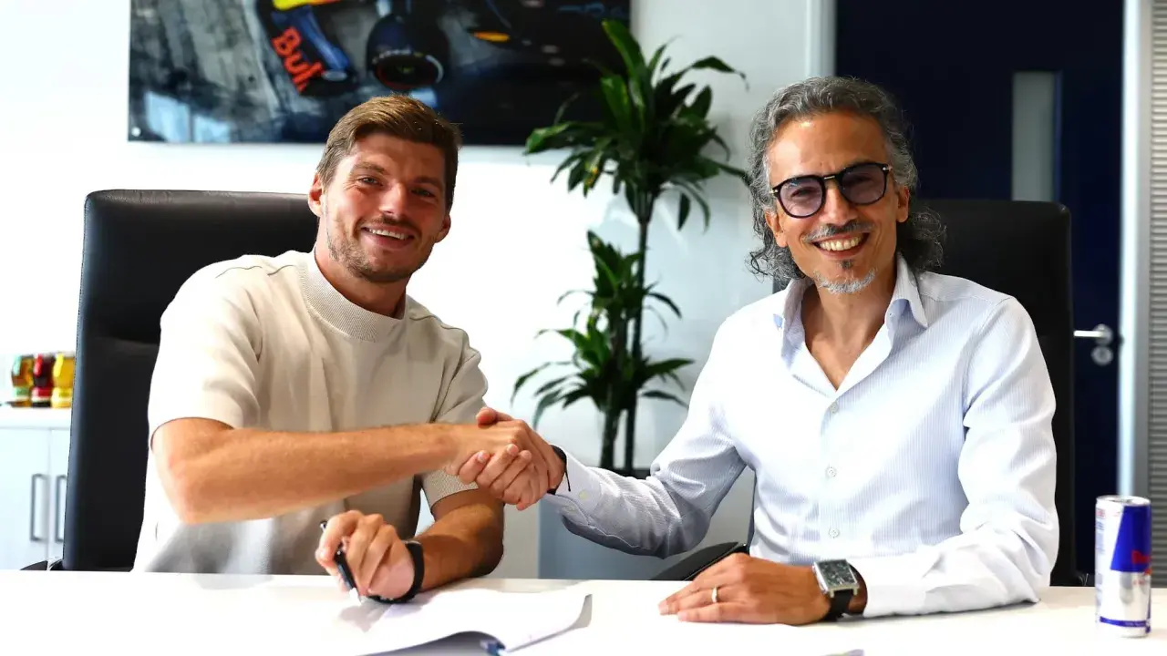 Max Verstappen sonríe mientras estrecha la mano de un hombre con gafas, sellando un acuerdo.