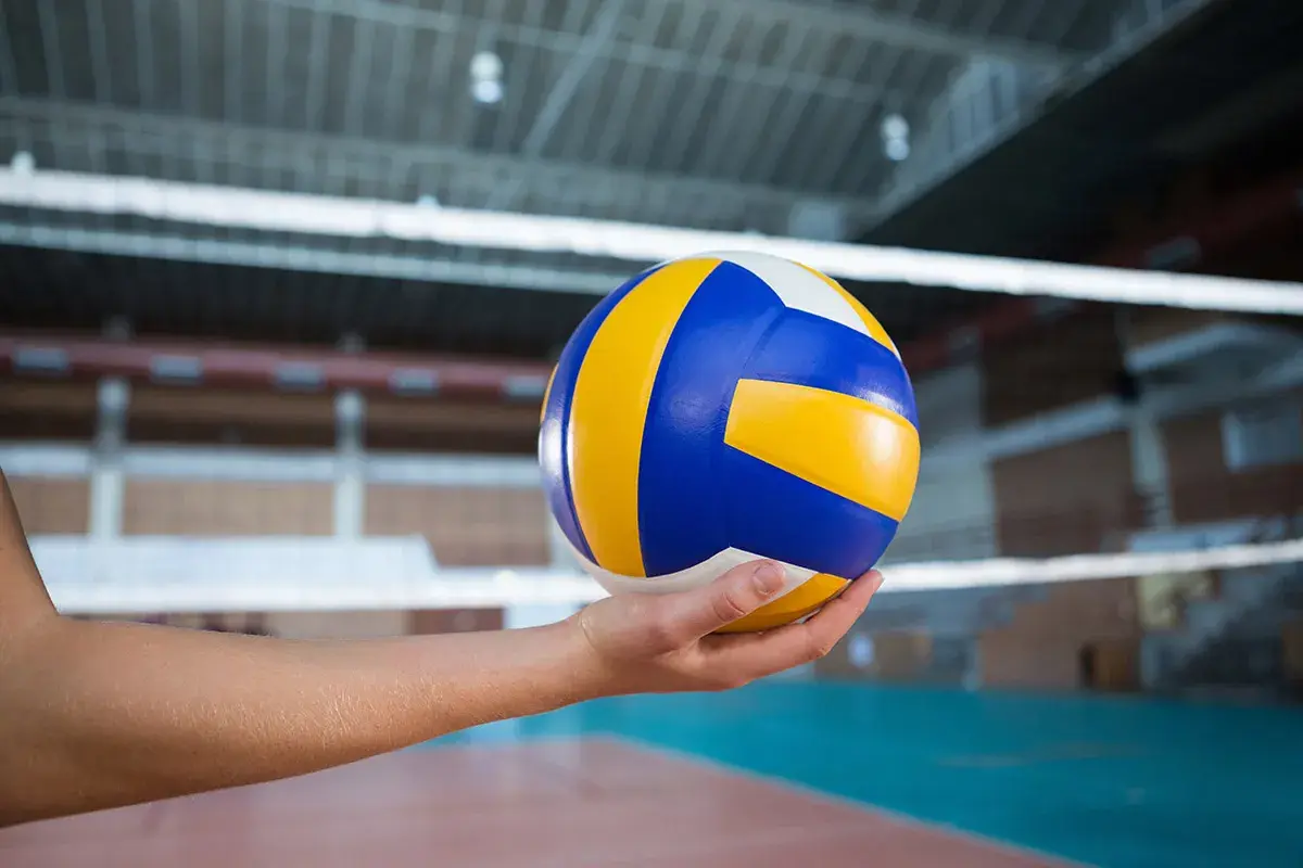 Piłka do siatkówki w dłoni, gotowa do zagrania nad siatką w hali sportowej.