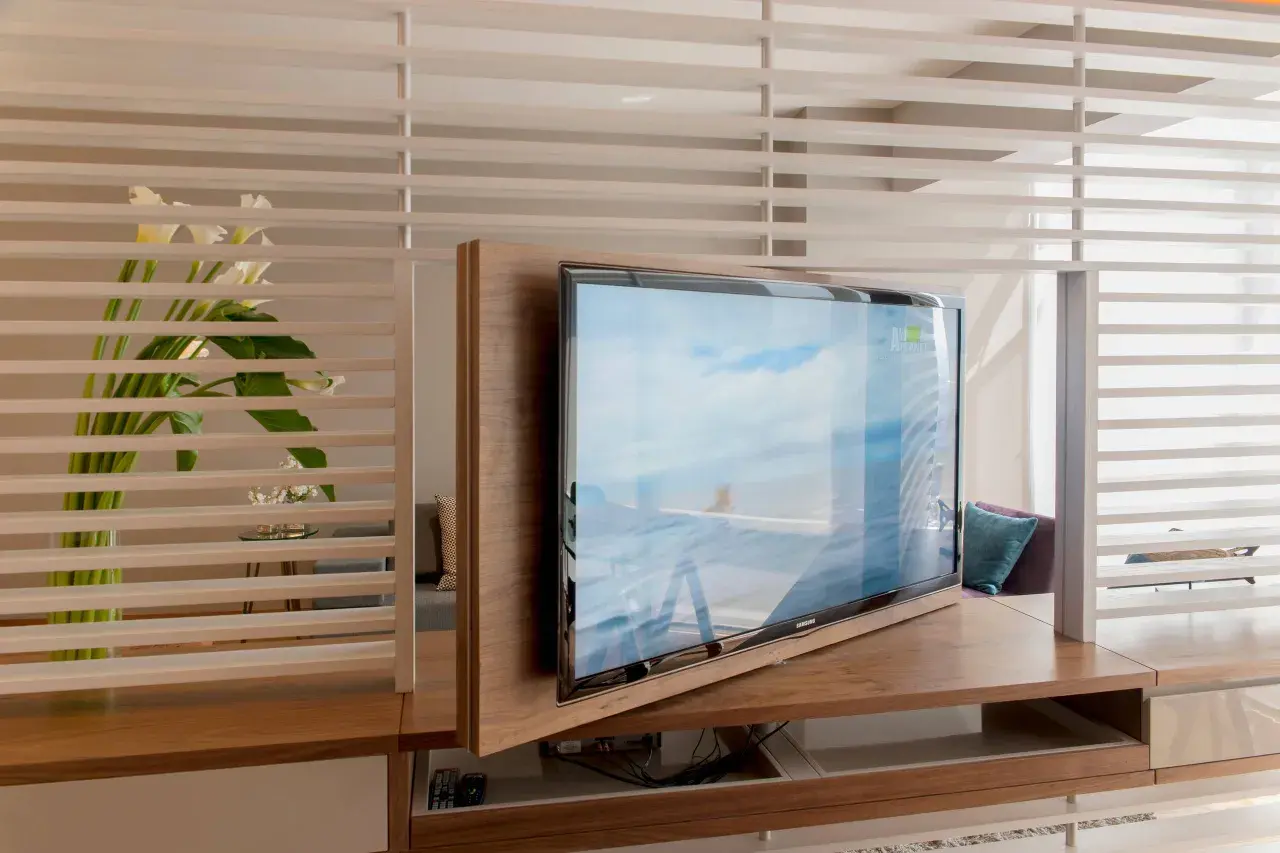 Ein moderner Wohnraum mit einem drehbaren Fernseher, der sich elegant in die Holzverkleidung integriert. Callas und dezente Beleuchtung schaffen eine ruhige Atmosphäre, ideal, um den Fernseher verstecken zu können.