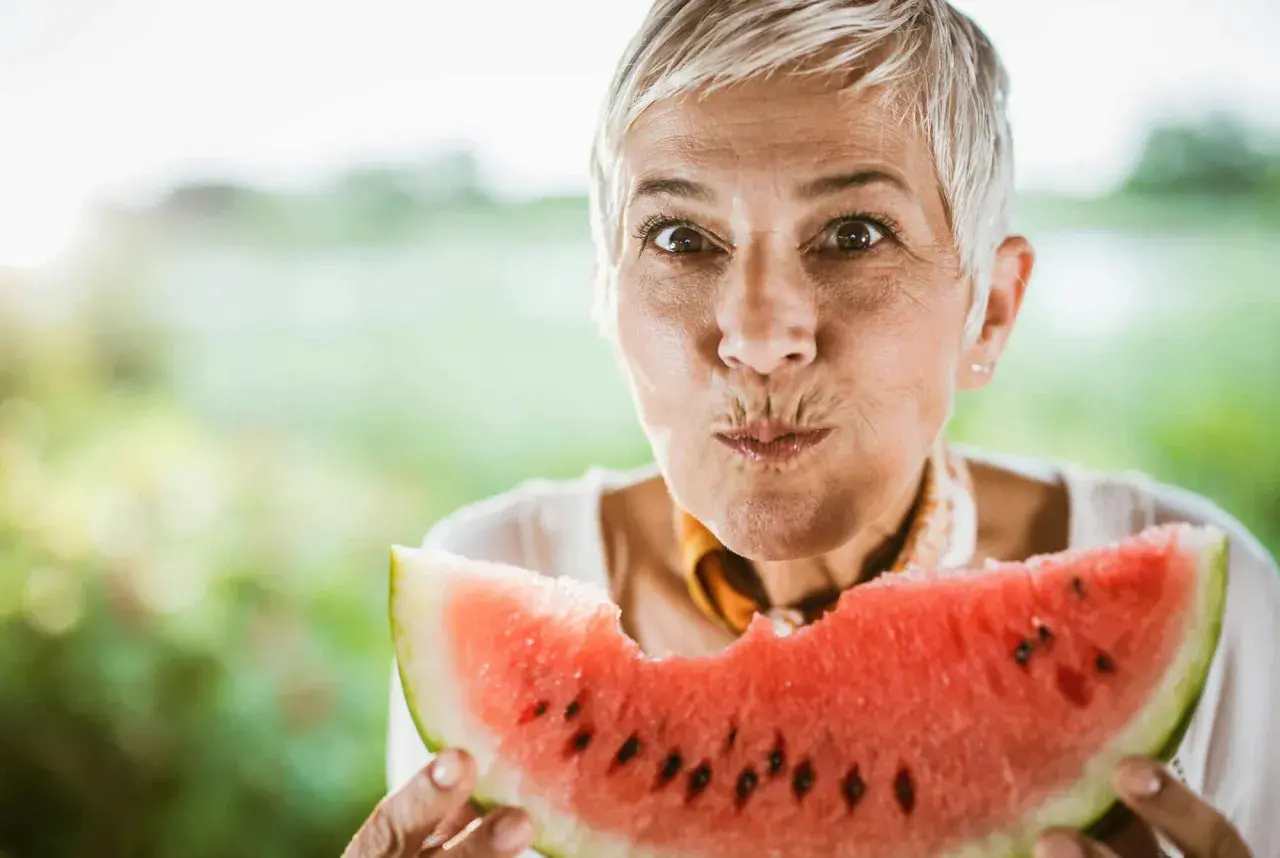 Glad kvinna med grått hår njuter av en saftig vattenmelon. Perfekt för ett uppfriskande vattenmelon recept.