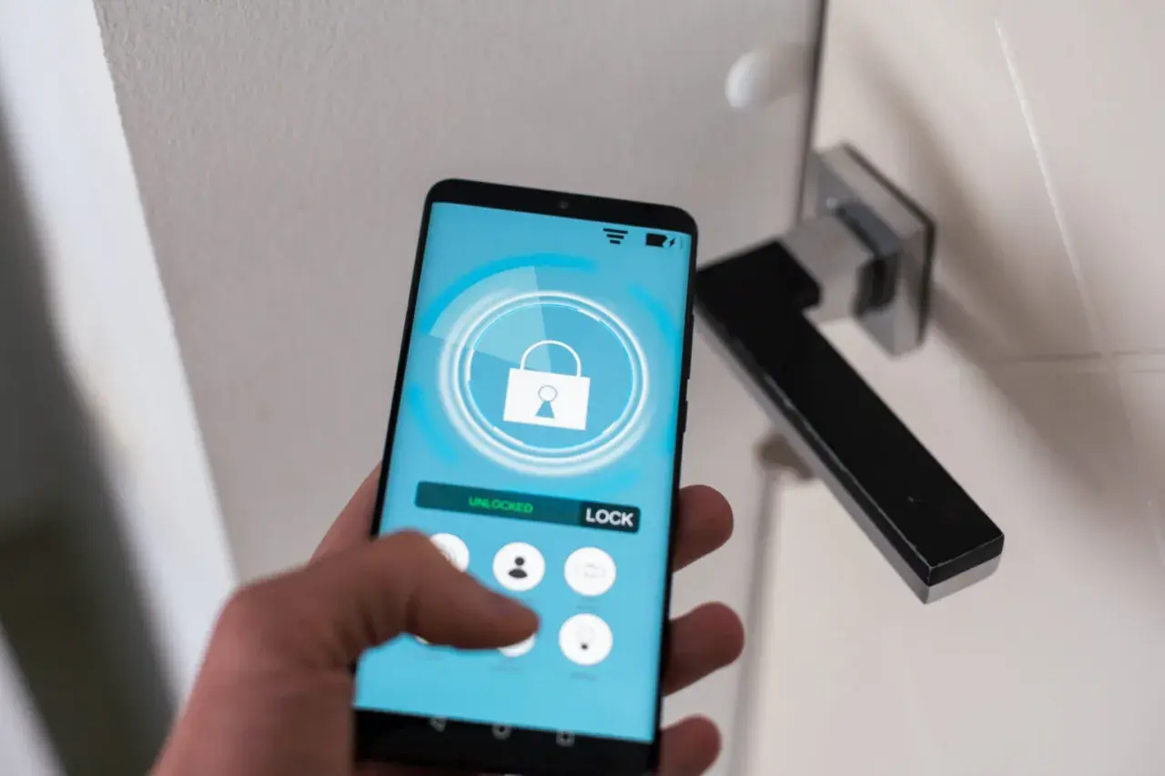 Dłoń trzyma smartfon z aplikacją do zdalnego sterowania zamkiem. Wygodny self check-in bez klucza.