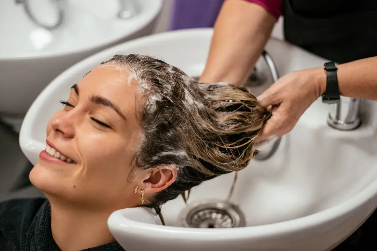 Una mujer sonríe mientras le lavan el pelo en un salón. La frecuencia con la que hay que lavarse el pelo varía, pero este momento de spa parece perfecto.