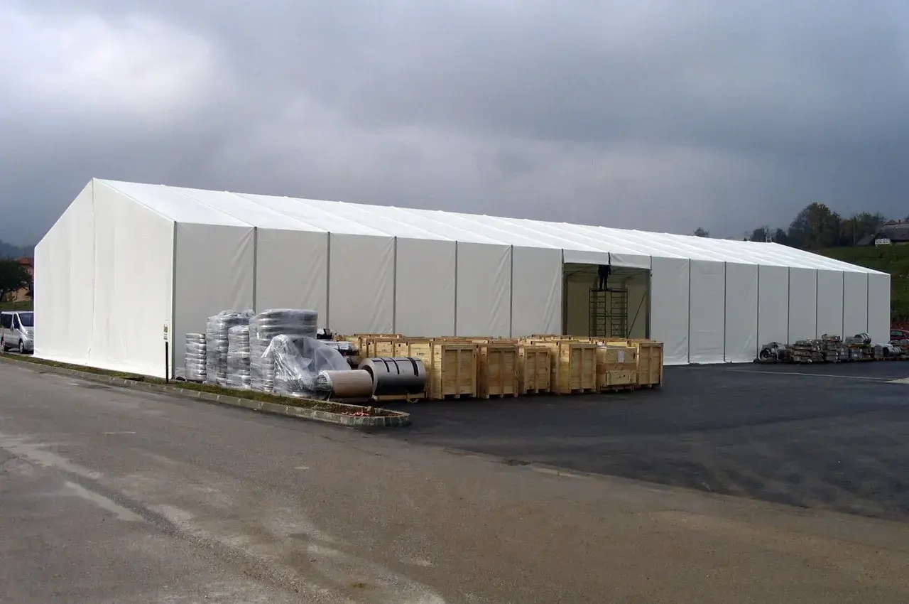 Ampia tensostruttura bianca, con merci stoccate all'esterno. Ottenere i permessi per queste strutture è fondamentale per la logistica.
