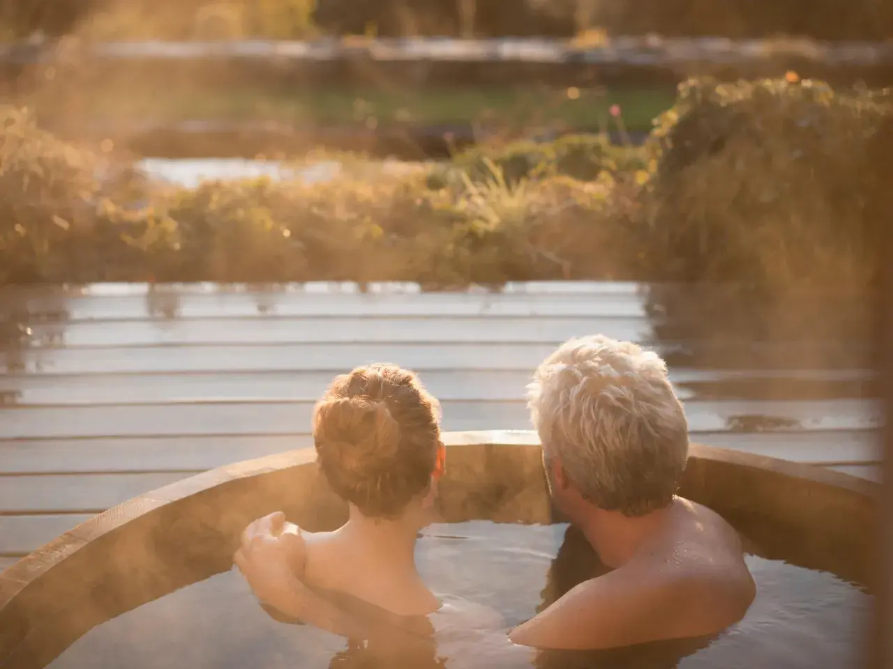 Pareja disfrutando de una relajante experiencia en un jacuzzi al atardecer. El vapor se eleva mientras se abrazan, creando un momento íntimo.
