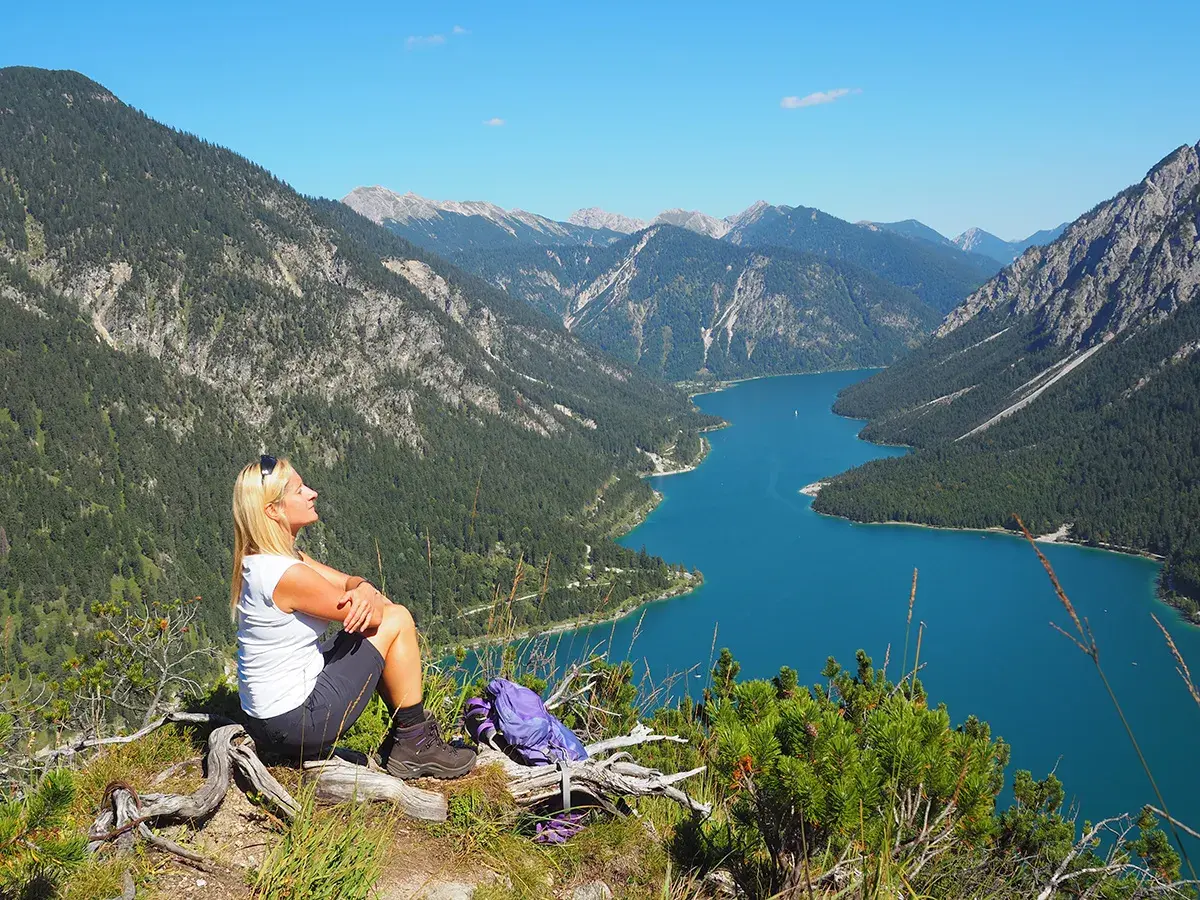Frau genießt Ausblick beim Plansee Wandern. Türkiser See, grüne Berge und blauer Himmel.