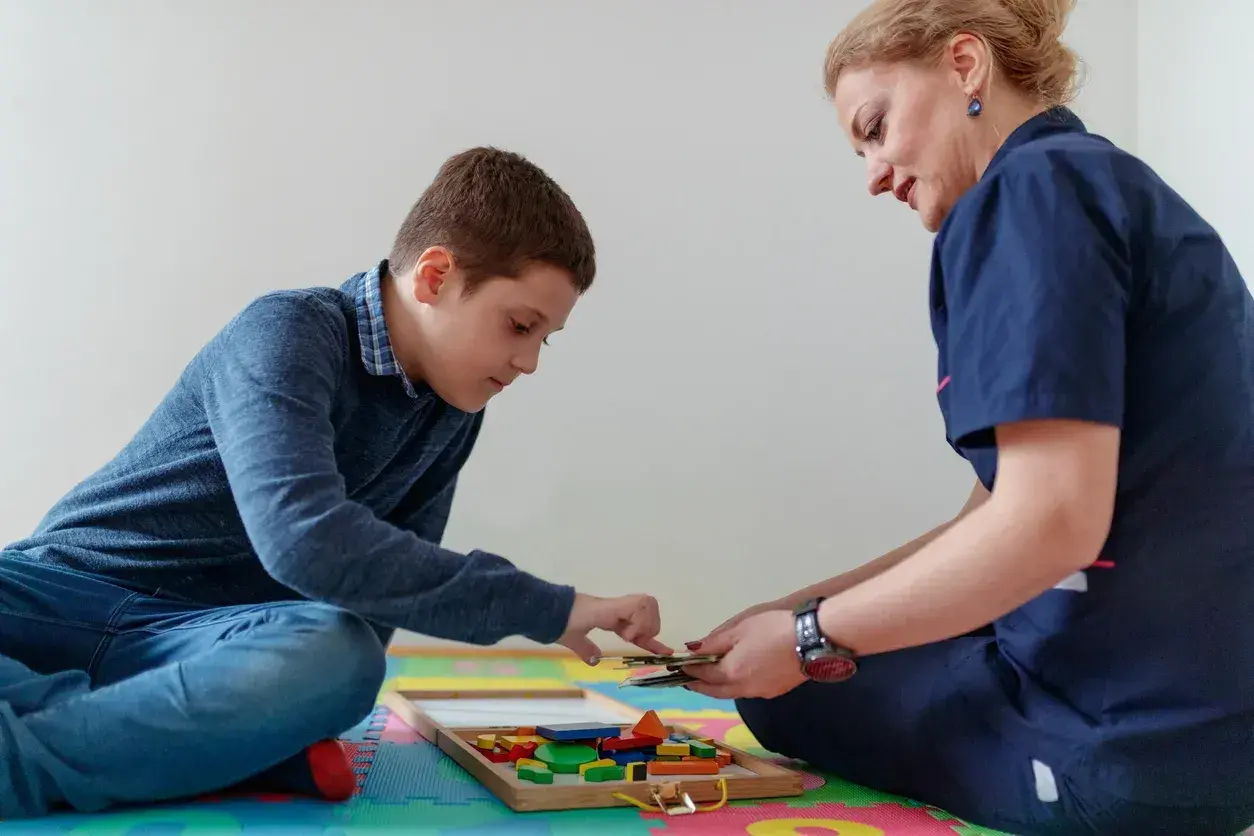 Chłopiec i terapeutka bawią się klockami w sali terapeutycznej.