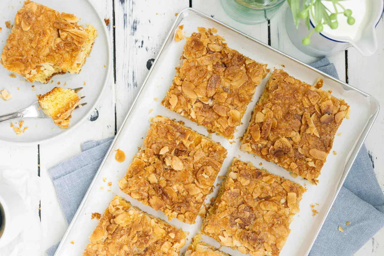 Saftiger butterkuchen ohne hefe, bestreut mit knusprigen Mandelblättchen. Ein Stück auf einem Teller mit einer Gabel.