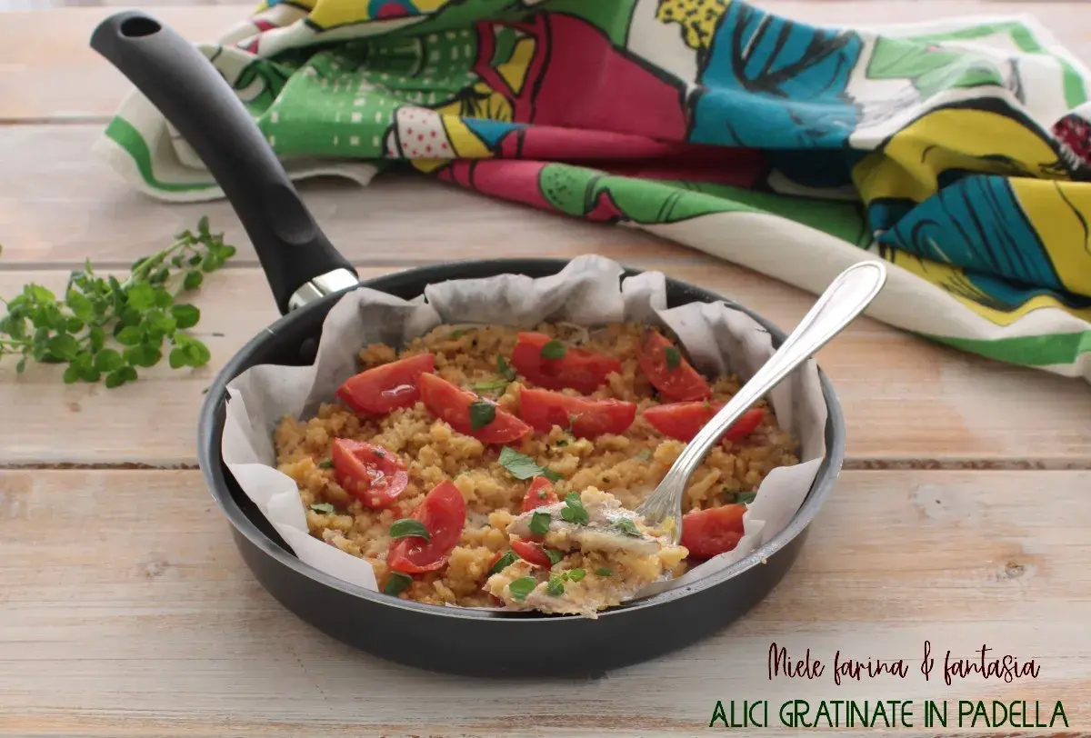 Alici gratinate in padella con pomodorini e pangrattato, un piatto semplice e gustoso.