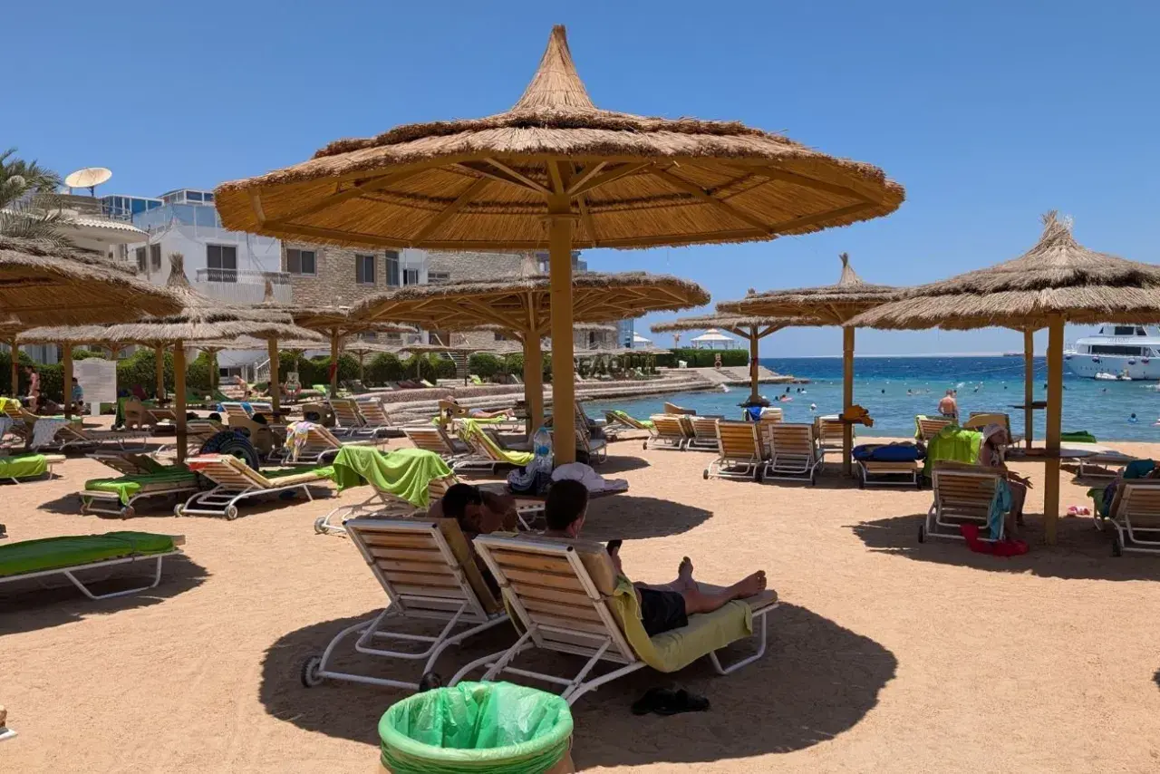 Egipt last minute all inclusive najtaniej: piaszczysta plaża z leżakami i parasolami, turkusowe morze, hotel w tle. Idealne miejsce na relaks.