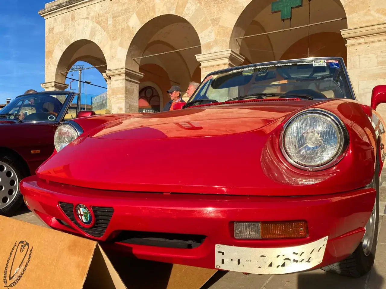 Dreaming of renting a car in Italy? This classic red Alfa Romeo convertible, parked under arched buildings, evokes the perfect Italian road trip.