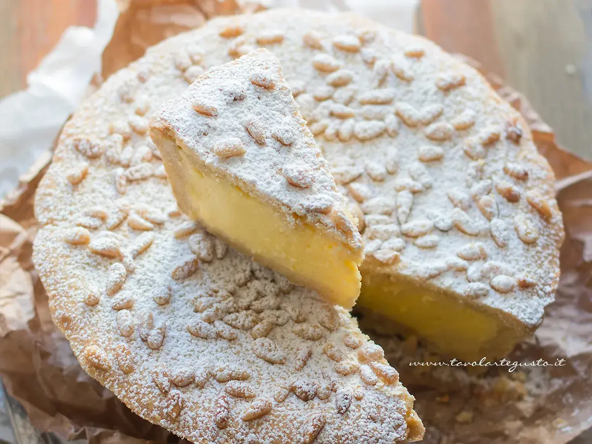 Una fetta di torta della nonna, cosparsa di pinoli e zucchero a velo, mostra il suo ripieno cremoso.