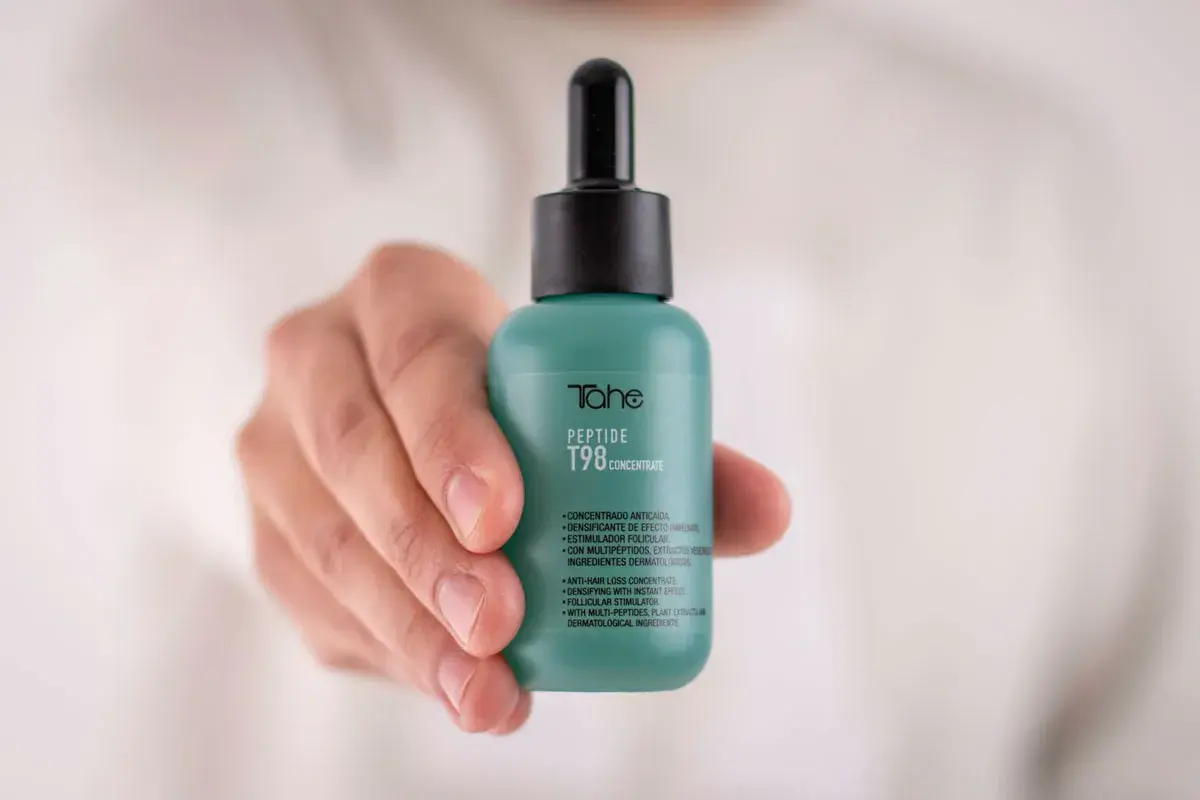 Mano sostiene frasco verde con peptidos para el pelo, concentrado anticaída T98 de Tahe.