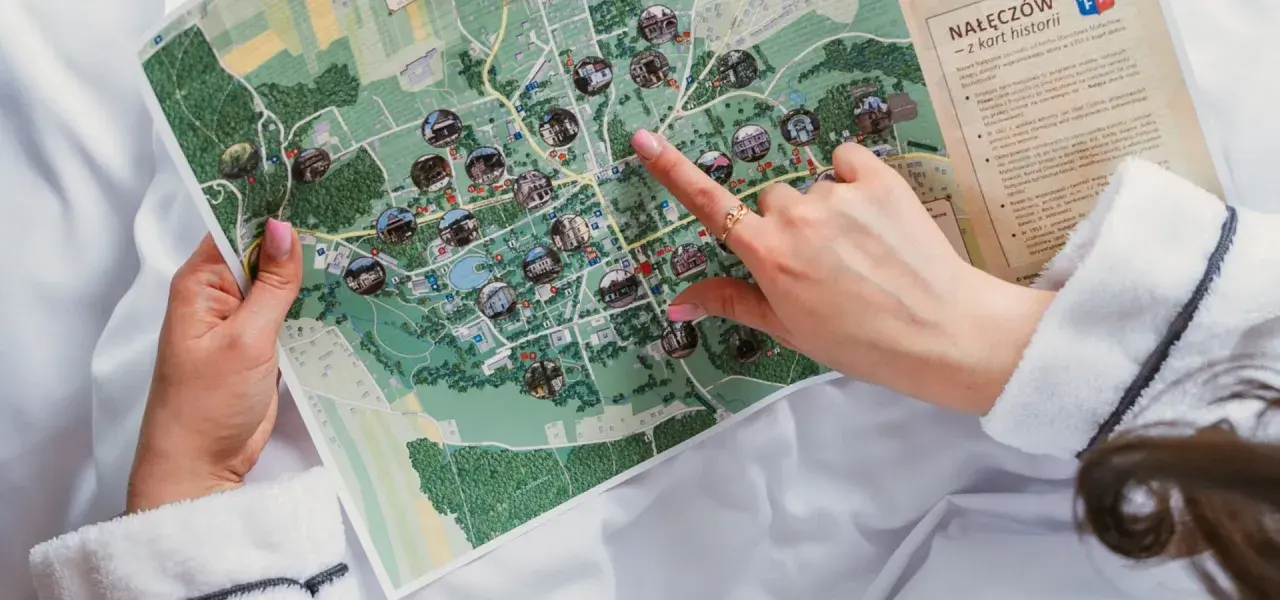 Ręka wskazuje na mapę Nałęczowa, pokazującą zabytki i atrakcje. Mapa przypomina o historii wszystkich województw w Polsce.