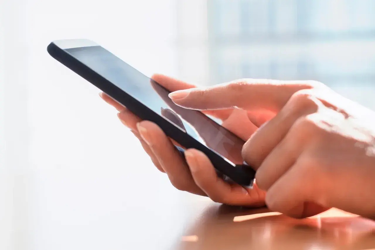 Dłoń dotyka ekranu smartfona, szukając archiwum SMS.