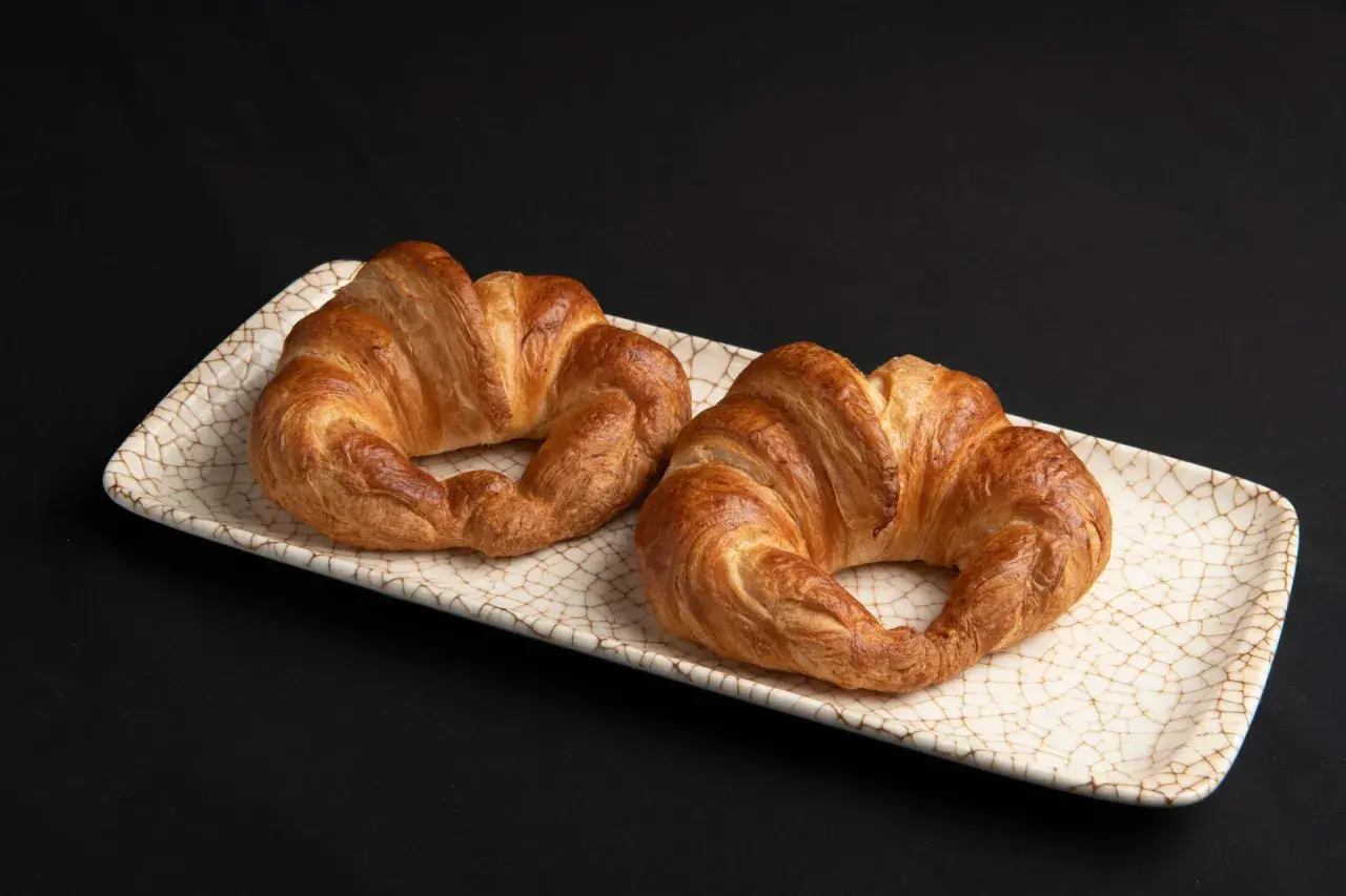 Dos croissants dorados, listos para disfrutar. El hojaldre crujiente invita a hacer croissant con hojaldre casero.