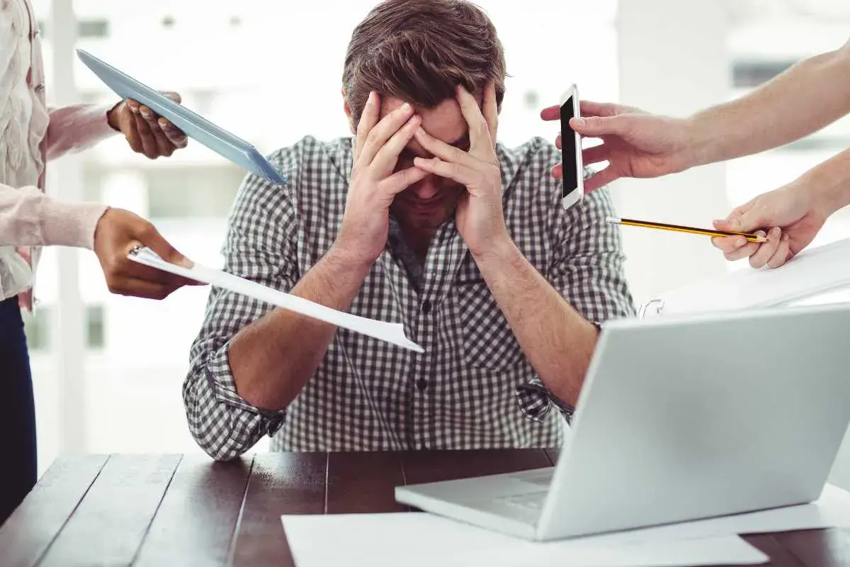 Uomo stressato, sommerso da richieste: tablet, fogli, telefono, matita. Il superlativo di busy è qui.
