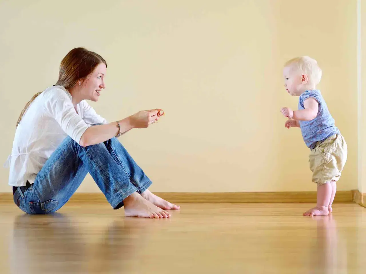 Mamma incoraggia il suo bambino, che sta imparando quando iniziano a camminare i bambini, a fare i suoi primi passi.