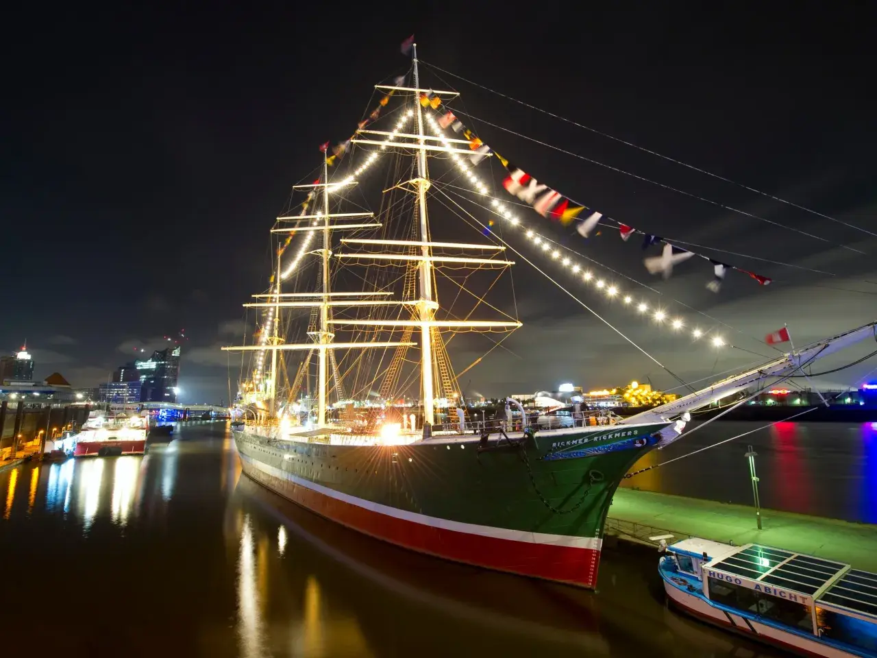 Großes Segelschiff mit Lichterketten und Flaggen im Hamburger Hafen bei Nacht, ein Highlight der museumsnacht hamburg.