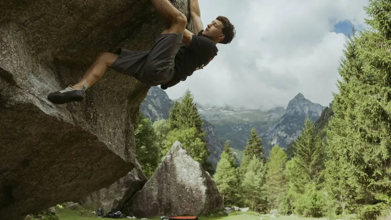 Mężczyzna wspina się po skale w górach, stosując zasady boulderingu. W tle piękne krajobrazy.