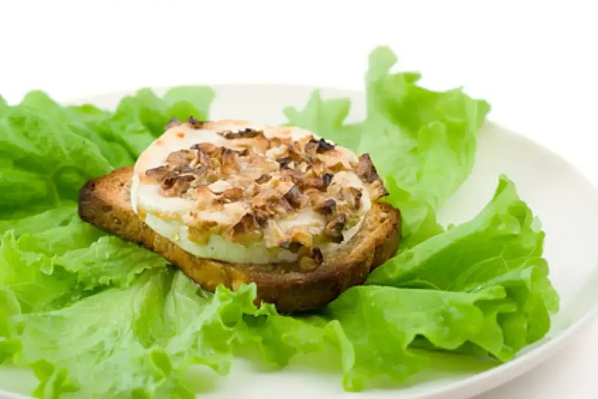 Tartine de chèvre chaud, garnie de noix, sur un lit de laitue fraîche. Un délice simple, comme un chevre au barbecue.