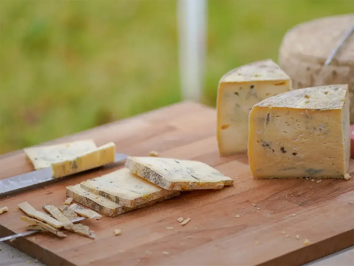 Formaggio stagionato con venature di muffa blu e verde su un tagliere di legno. Alcune fette sono già state tagliate.