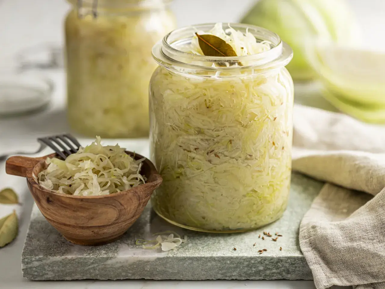Frisches Sauerkraut im Glas, bereit für ein leckeres Sauerkraut Rezept. Ein kleiner Holzlöffel mit Sauerkraut und Lorbeerblätter liegen daneben.