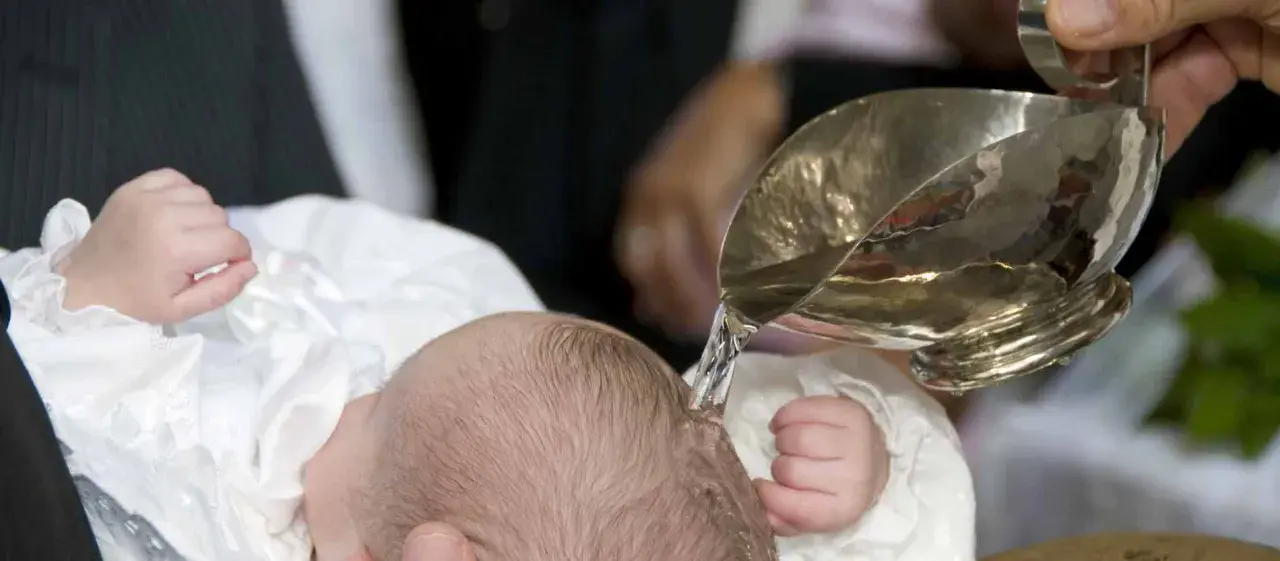 Taufe eines Babys mit Wasser aus einem silbernen Gefäß.