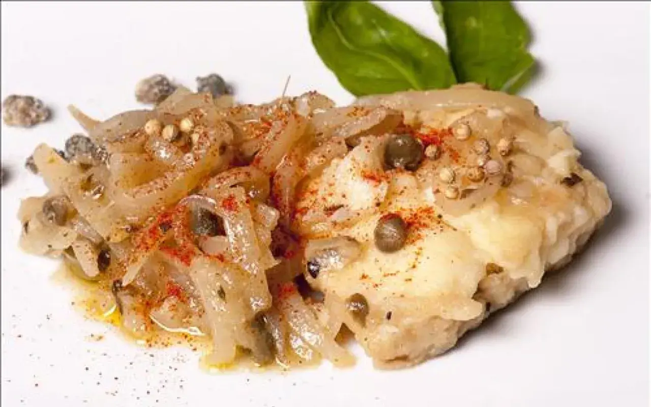 Un morceau de lotte poisson, cuisiné avec des oignons, des câpres et des épices, garni de feuilles de basilic.