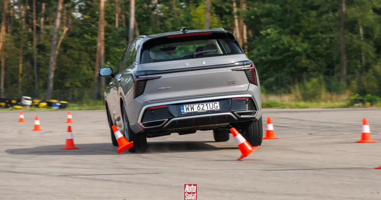 Szary SUV wykonuje test łosia, gwałtownie skręcając między pomarańczowymi pachołkami na torze.