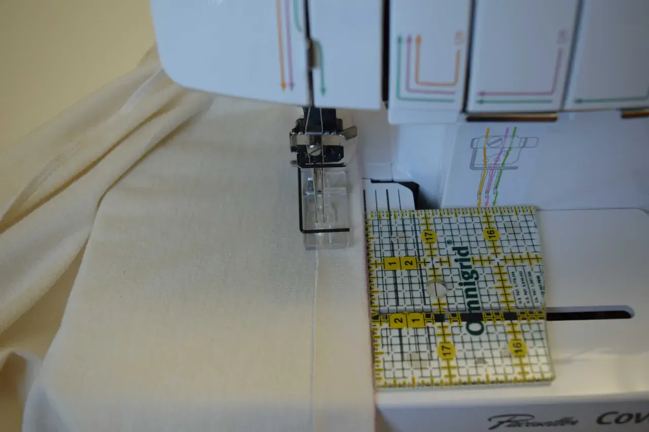 A ruler guides fabric under a coverstitch machine needle, showing how to use a coverstitch machine for precise hemming.