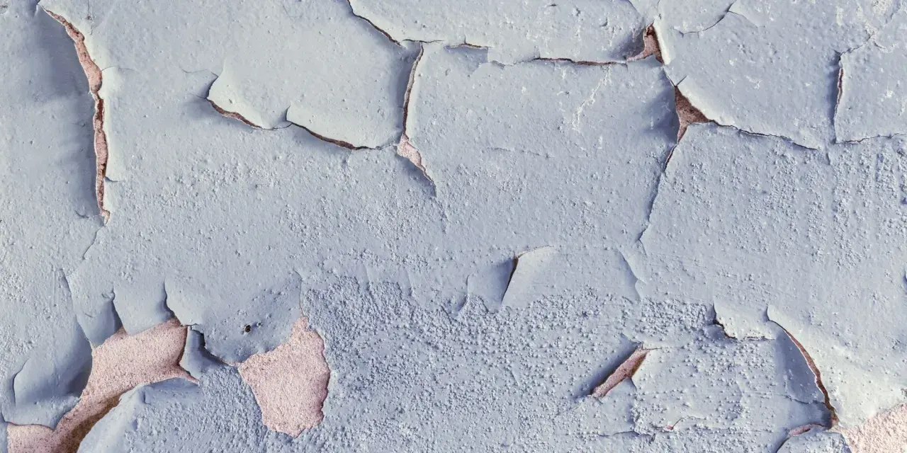 Texture d'une peinture qui s'écaille, révélant la texture rugueuse du mur sous-jacent, témoignant de l'humidité.
