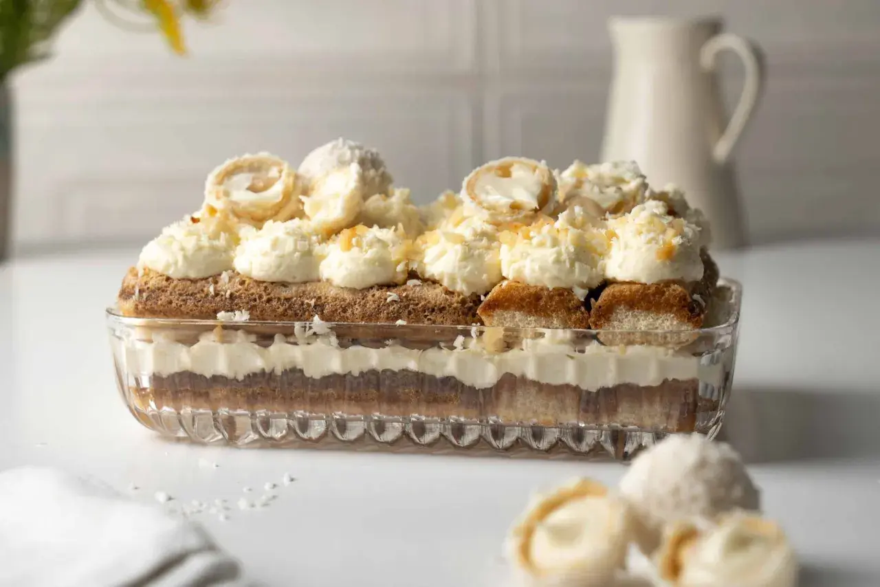 Ein Raffaello Tiramisu in einer Glasform, geschichtet mit Löffelbiskuits, Creme und Kokosraspeln. Obenauf dekorative Kokospralinen.