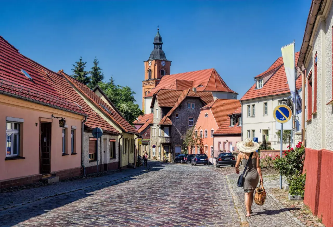 Idyllisches Dorf mit Kopfsteinpflasterstraße, Kirche und einer Frau mit Hut. Perfekt für Ausflugsziele Berlin Brandenburg.