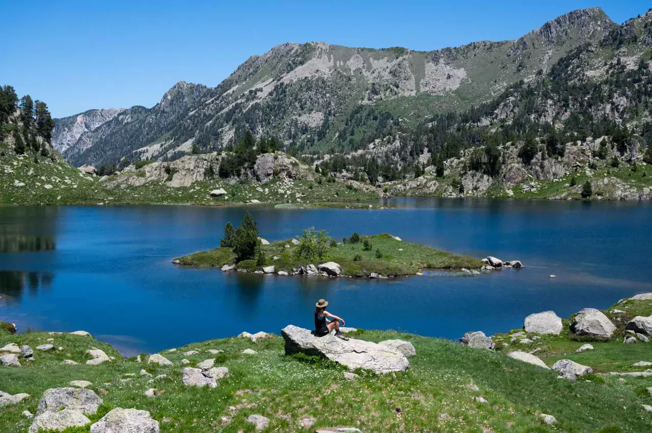 Persona sentada en roca contempla el azul intenso del circ de Colomers, rodeado de montañas verdes y un cielo despejado.