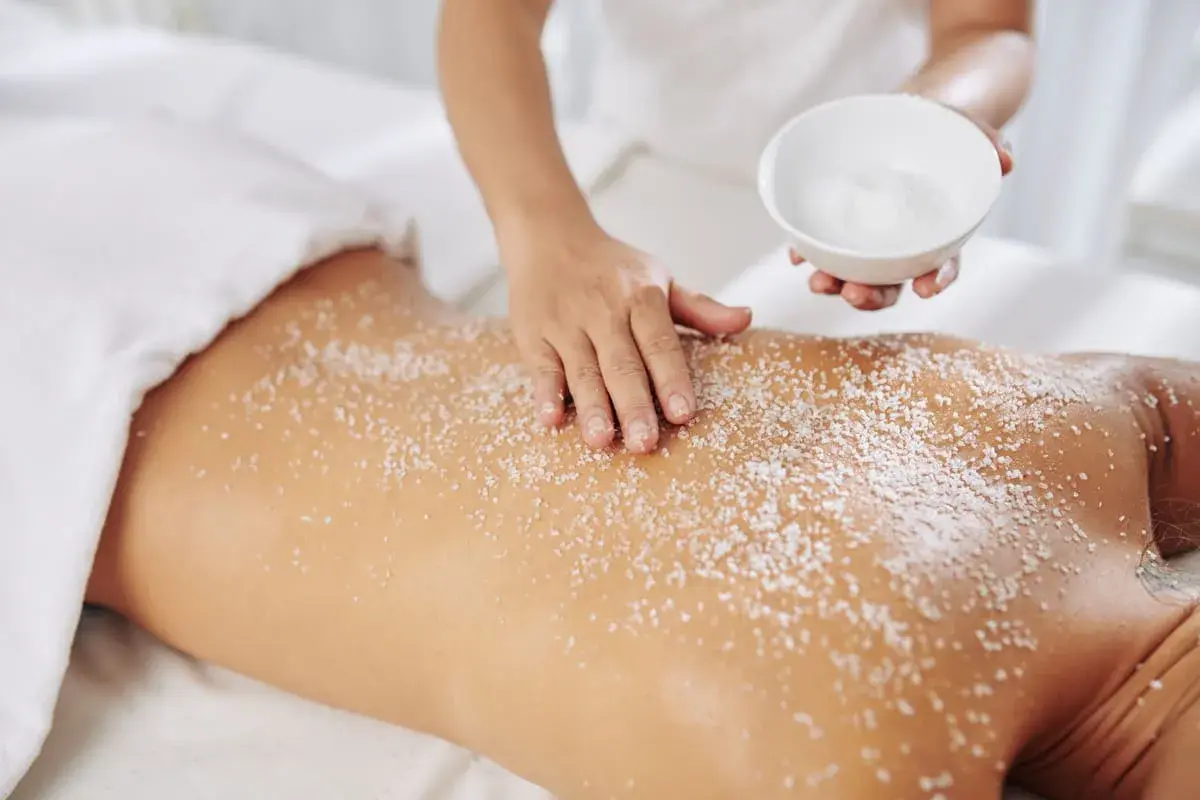 Mani esperte applicano un massaggio scrub con sale sulla schiena di una persona, per un'esfoliazione profonda e rigenerante.