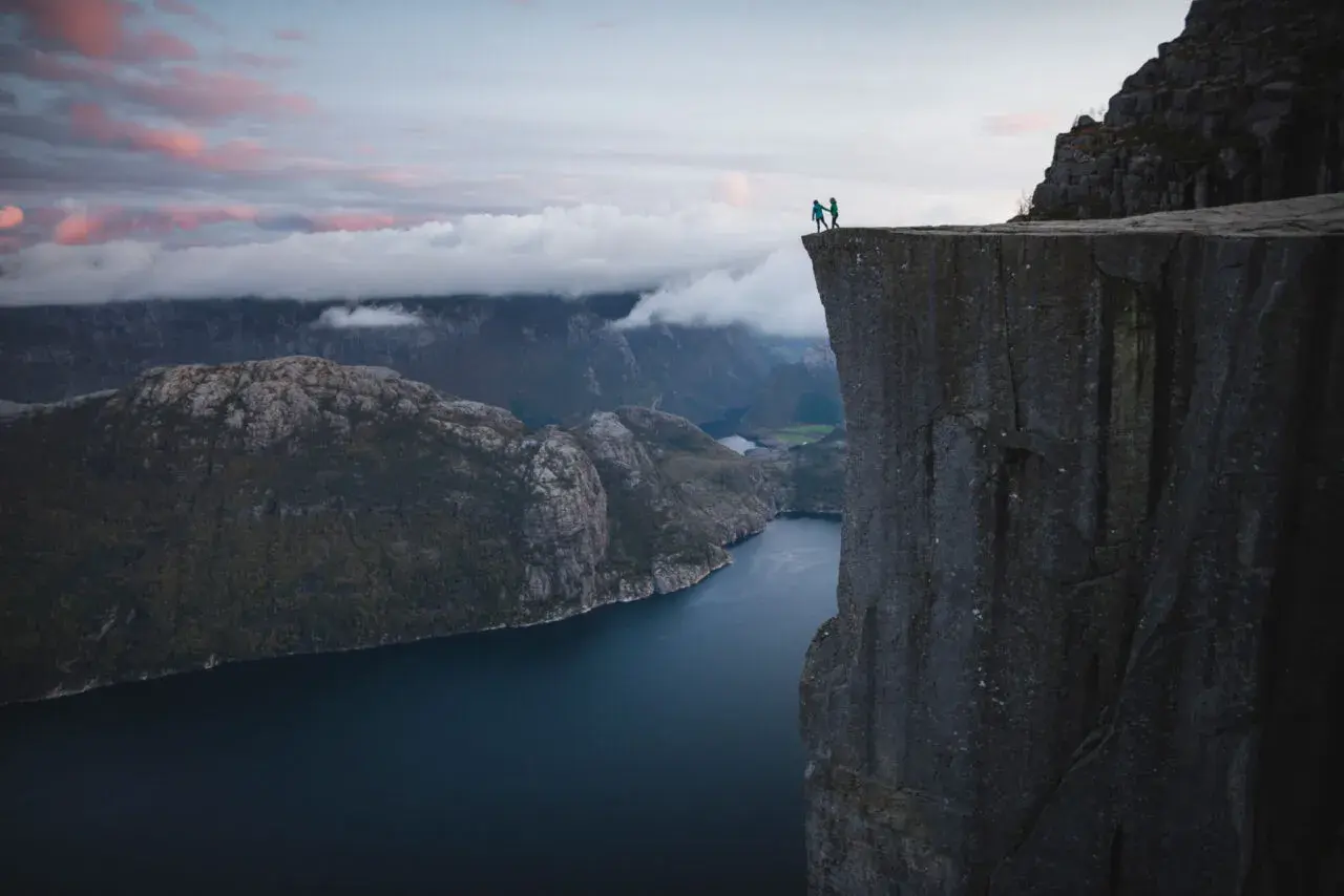 Två personer står på en klippavsats med hisnande utsikt över en fjord. Trots **höjdrädsla** vågar de sig nära kanten.
