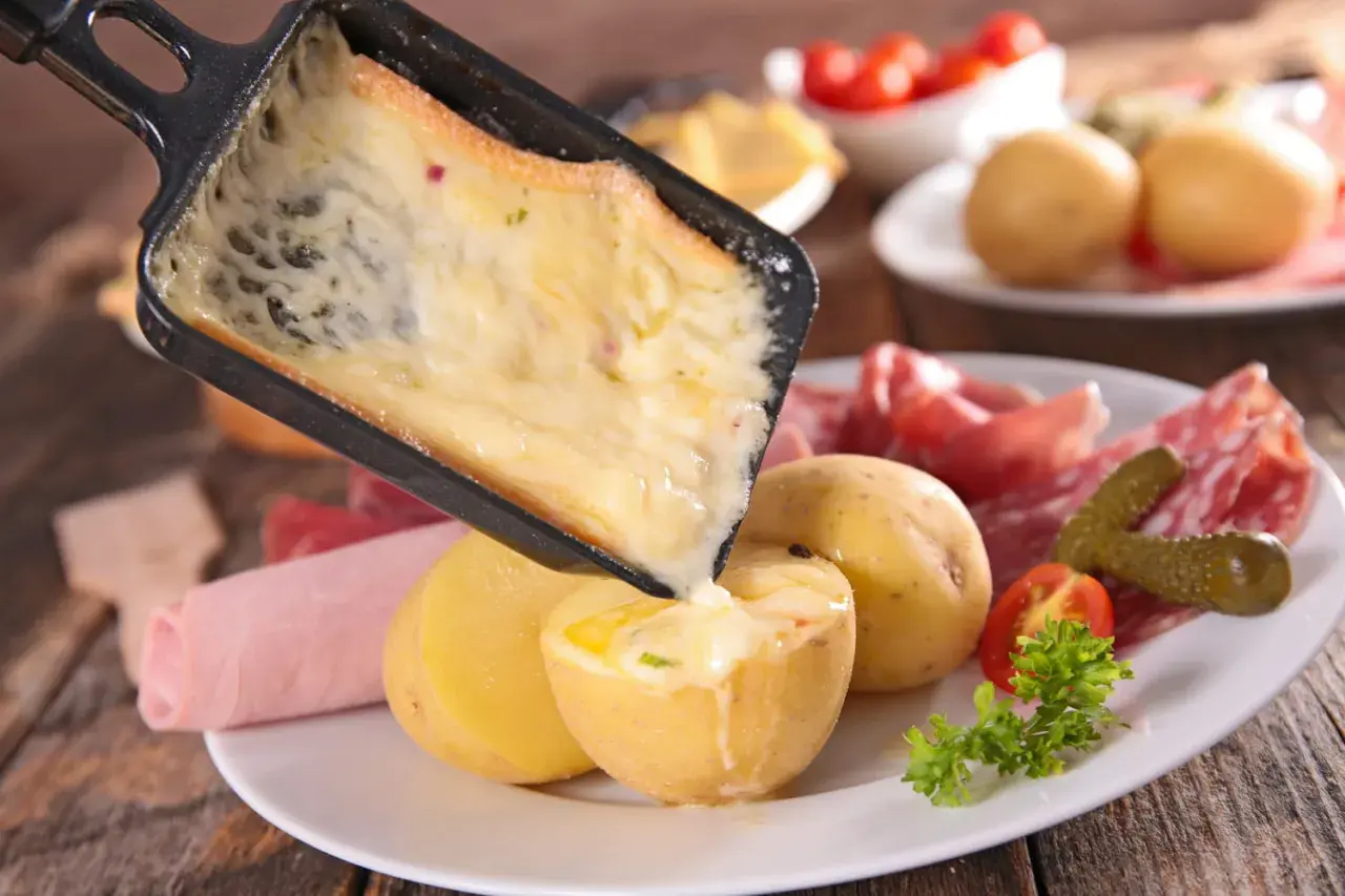 Une idée raclette originale : du fromage fondu coulant sur des pommes de terre, charcuterie et cornichons.