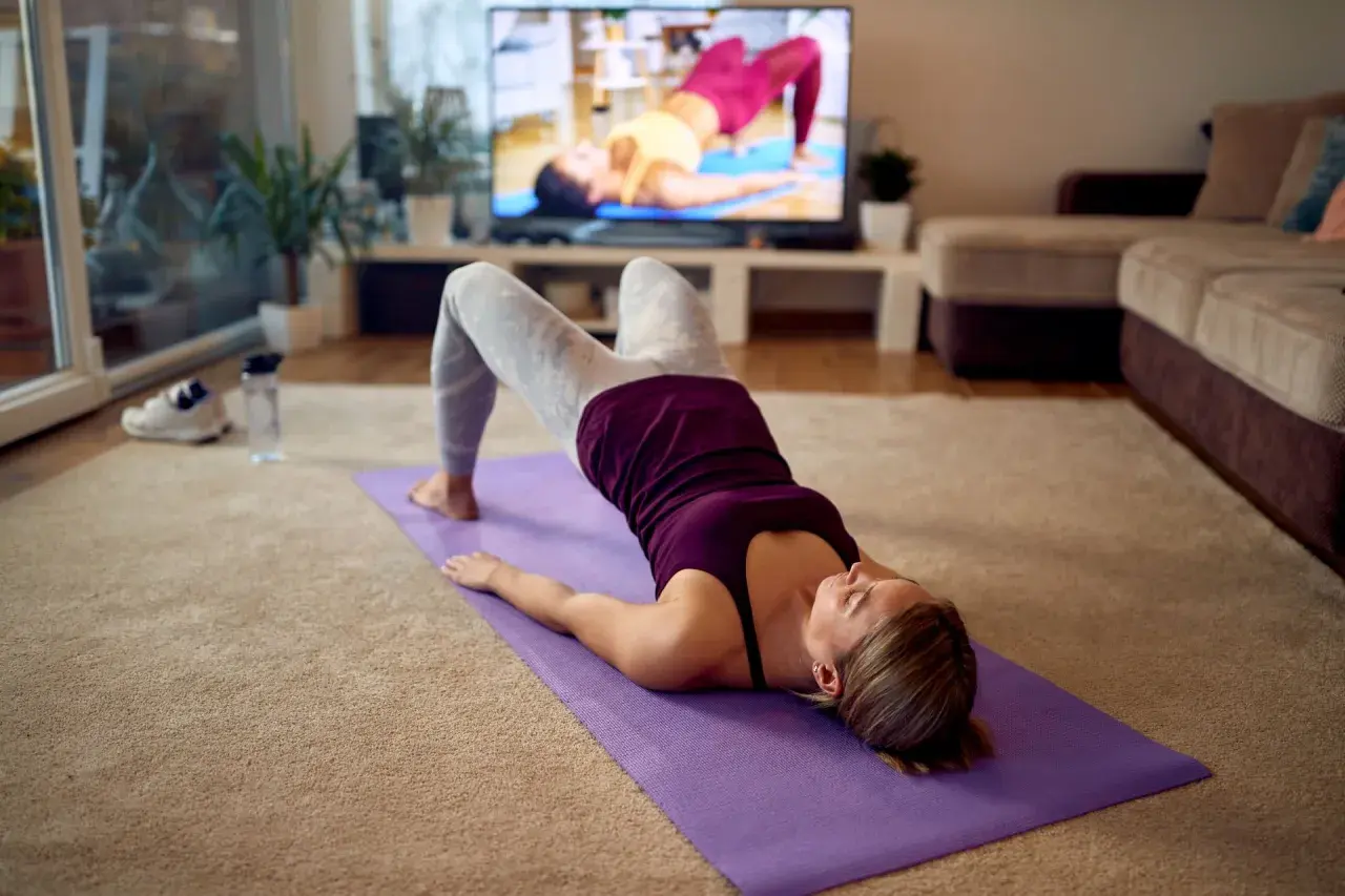 Mujer haciendo ejercicio en casa, buscando algo para el estreñimiento. Yoga en la alfombra frente a la TV.