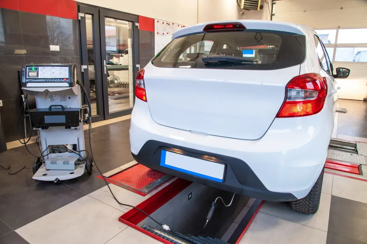 Controllo emissioni per la revisione auto scaduta. Un'auto bianca è collegata a un analizzatore di gas di scarico in un'officina.