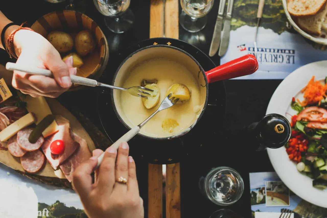 Un délicieux moment de partage autour d'une fondue savoyarde, accompagnée d'un verre de riesling. Des pommes de terre et de la charcuterie complètent ce festin.
