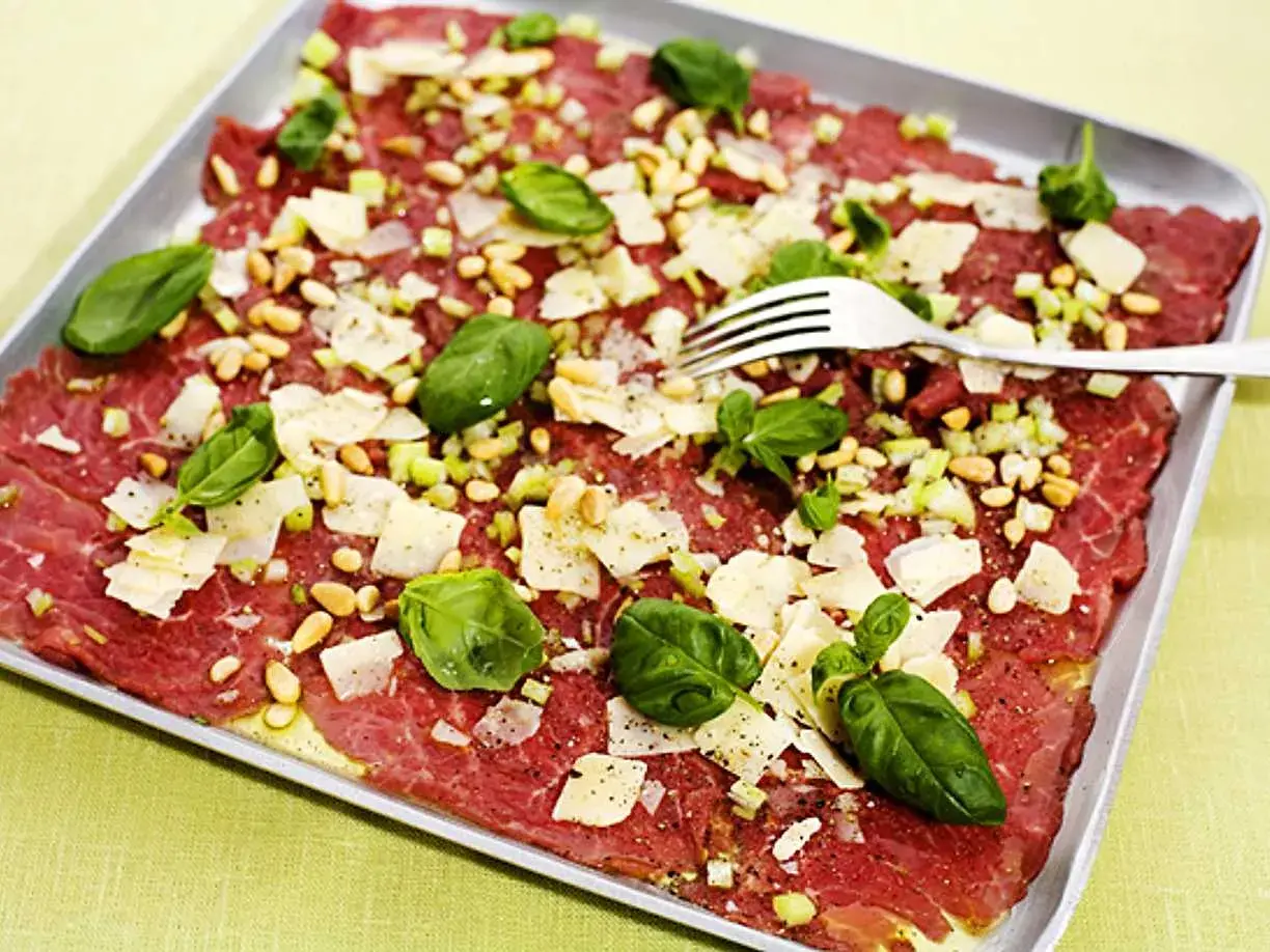 En läcker carpaccio med tunt skivat kött, pinjenötter, parmesan och basilika. Ett perfekt carpaccio recept för en förrätt.