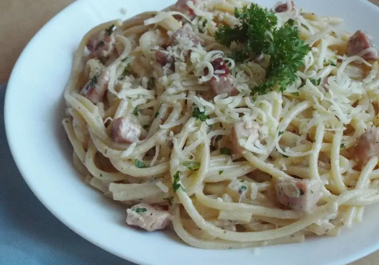 Pyszna, kremowa wloska carbonara z kawałkami boczku i posypana parmezanem, udekorowana natką pietruszki.