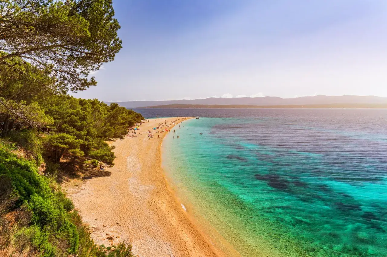Traumhafter kroatischer Strand mit Pinienwald und türkisfarbenem Wasser. Menschen entspannen sich am Zlatni Rat Strand.