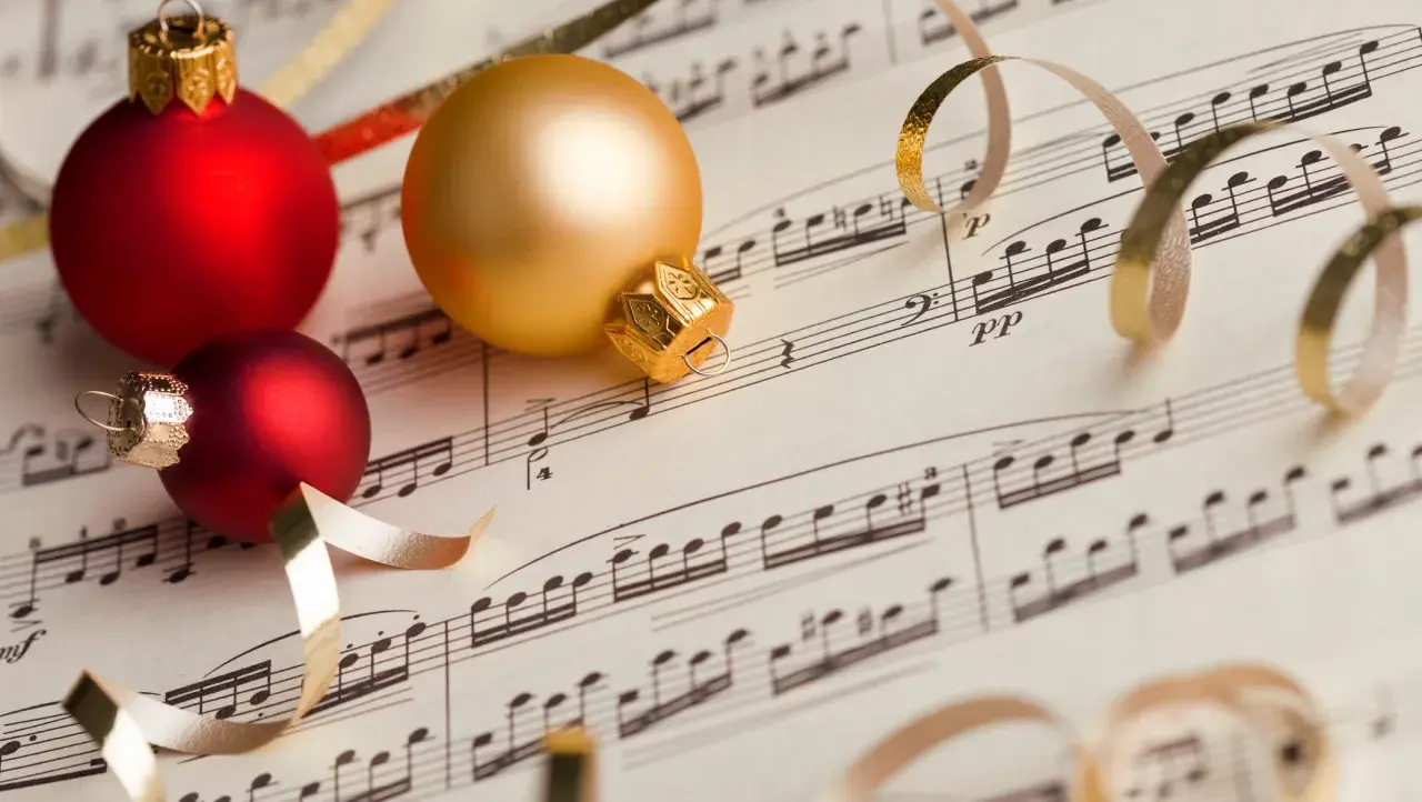 Palline rosse e dorate su spartito musicale, un'anticipazione delle 10 canzoni di Natale più popolari.