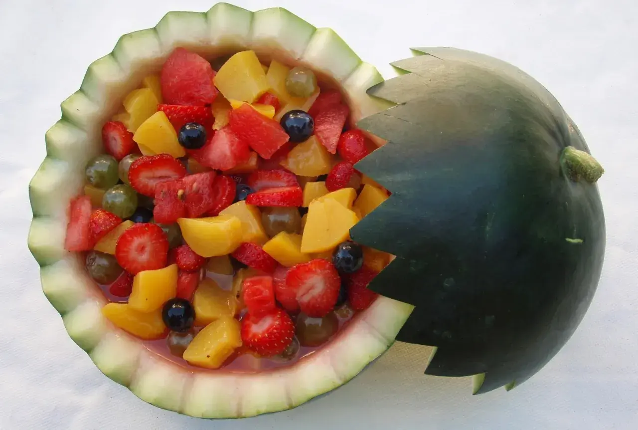 Deliciosa macedonia de frutas servida en una sandía tallada, con fresas, melocotón, uvas y arándanos.
