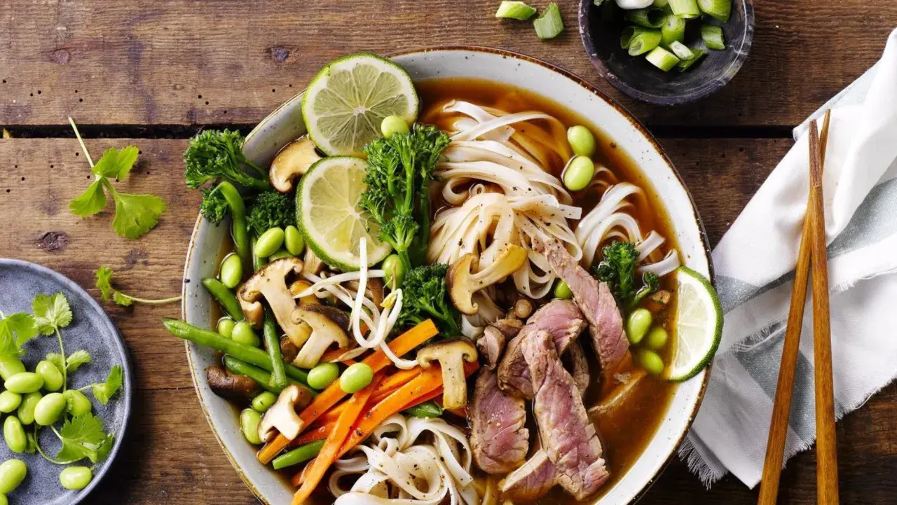 En skål med pho recept med nudlar, biff, grönsaker och lime.