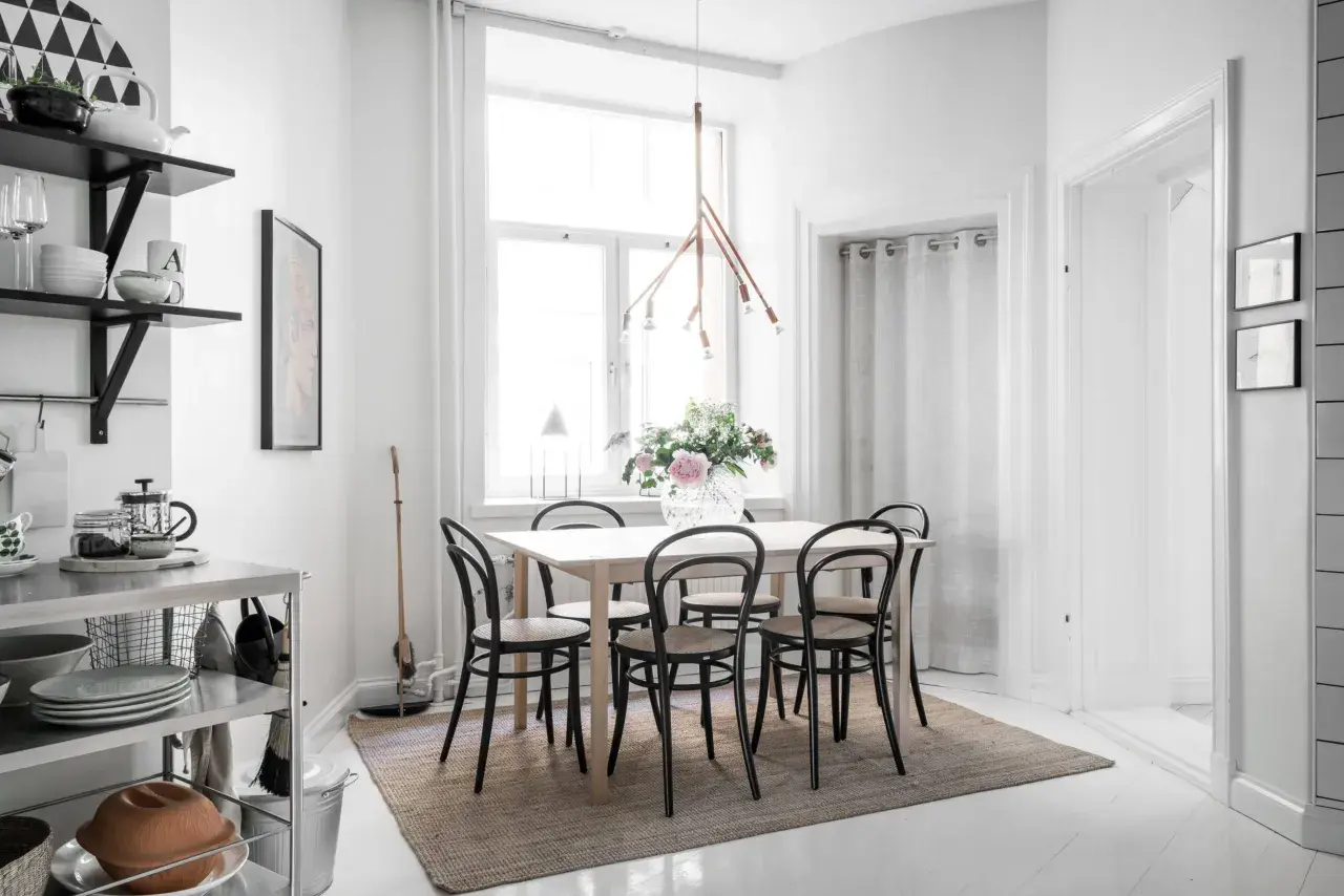 En ljus och mysig matplats med ett träbord, svarta stolar och en vacker blomsterbukett. En taklampa i trä ger ett varmt sken.