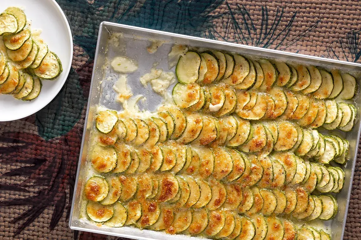 Fette di zucchine al forno con mozzarella filante, disposte in file ordinate in una teglia, pronte per essere gustate.