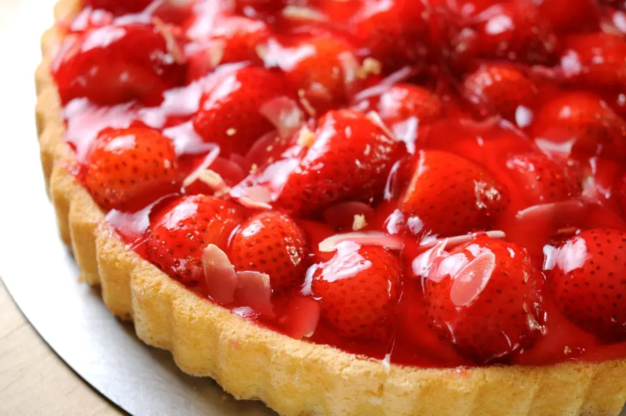 Una deliziosa torta di fragole, con fragole fresche e succose ricoperte da una lucida glassa rossa, su una base dorata.